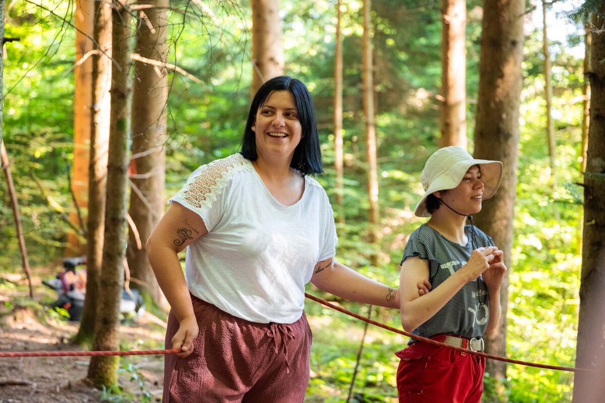 Eine Mitarbeiterin des Ateliers begleitet eine Klientin im Wald beim Spielen