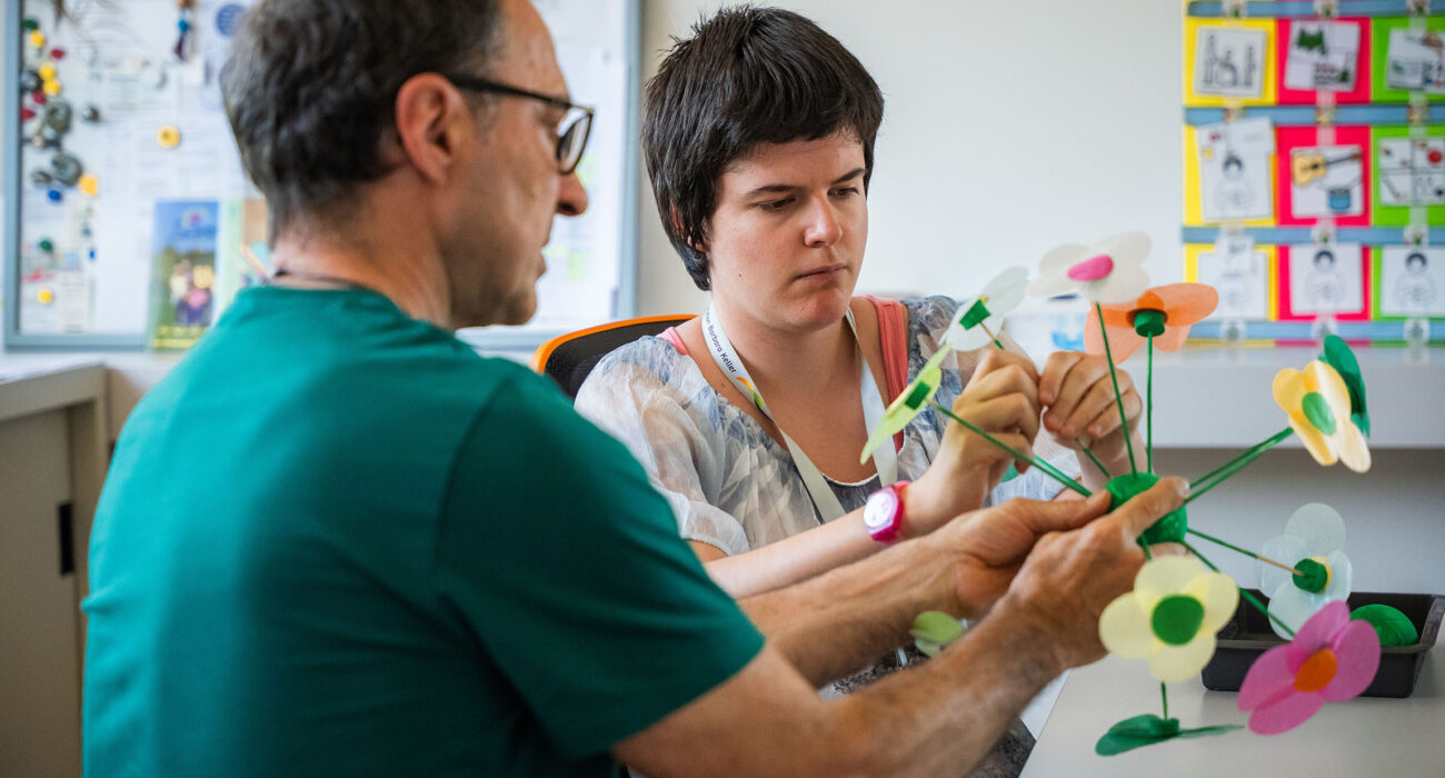 Ein Mitarbeiter des Ateliers hilft einer Klientin beim Basteln