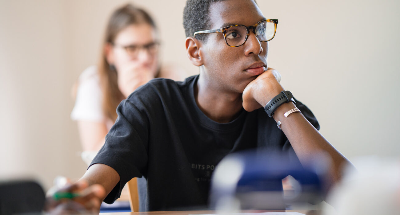 Ein Schüler sitzt am Schülerpult und sieht nachdenklich aus