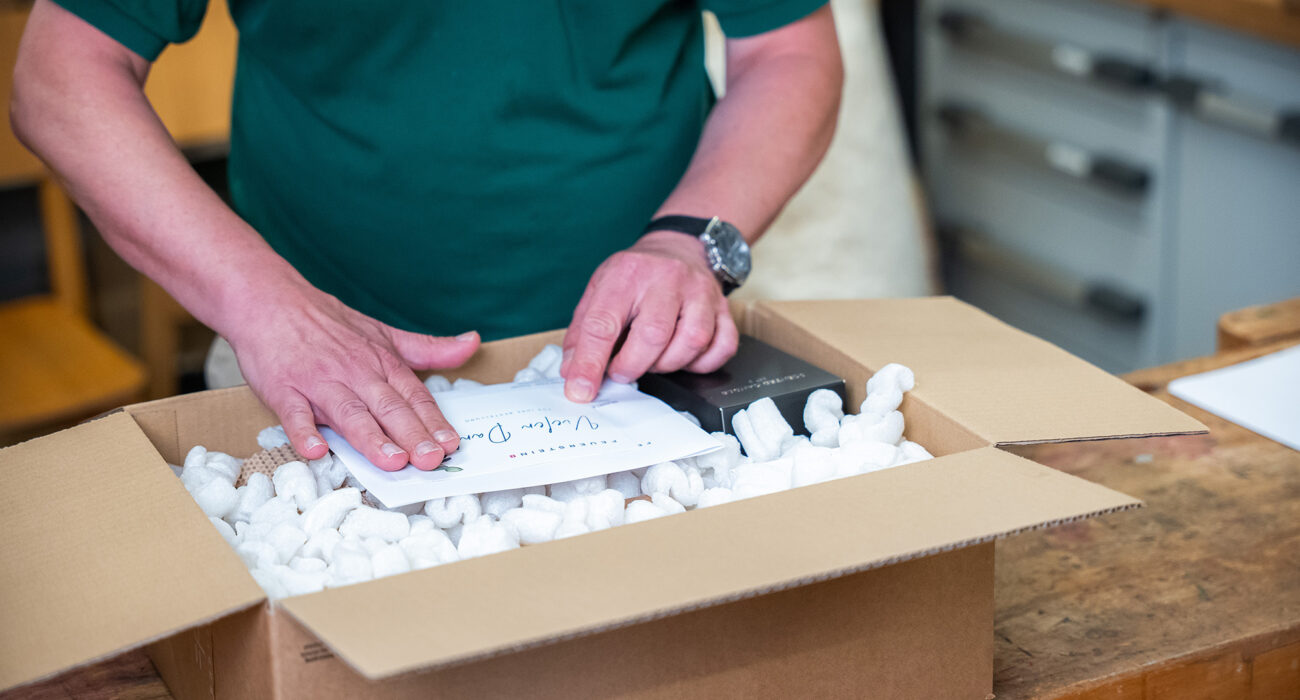 Hände verpacken ein Paket und legen einen Zettel dazu