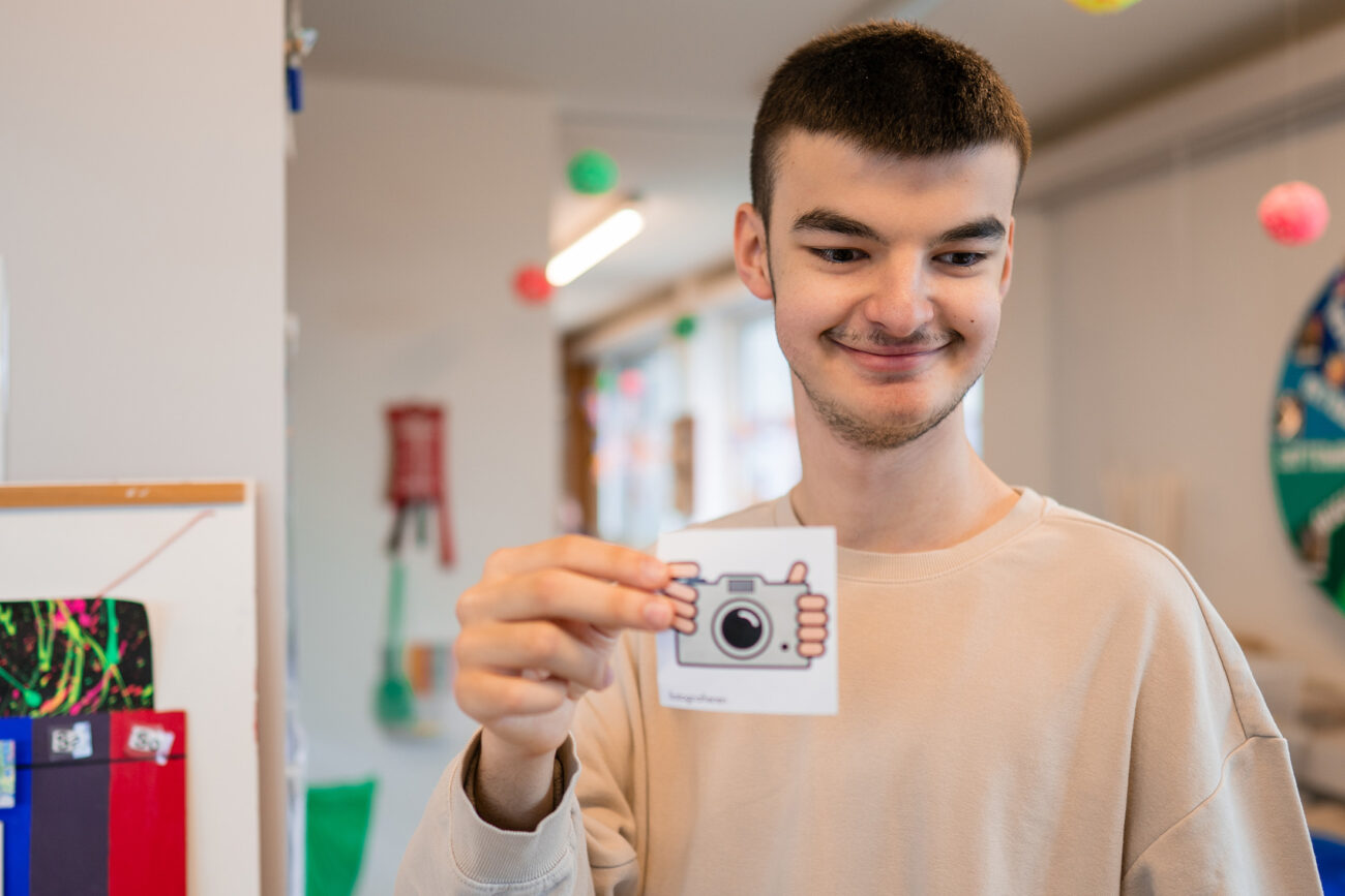 Ein Mitarbeiter des Ateliers hält ein Piktogramm mit einer Kamera in den Händen